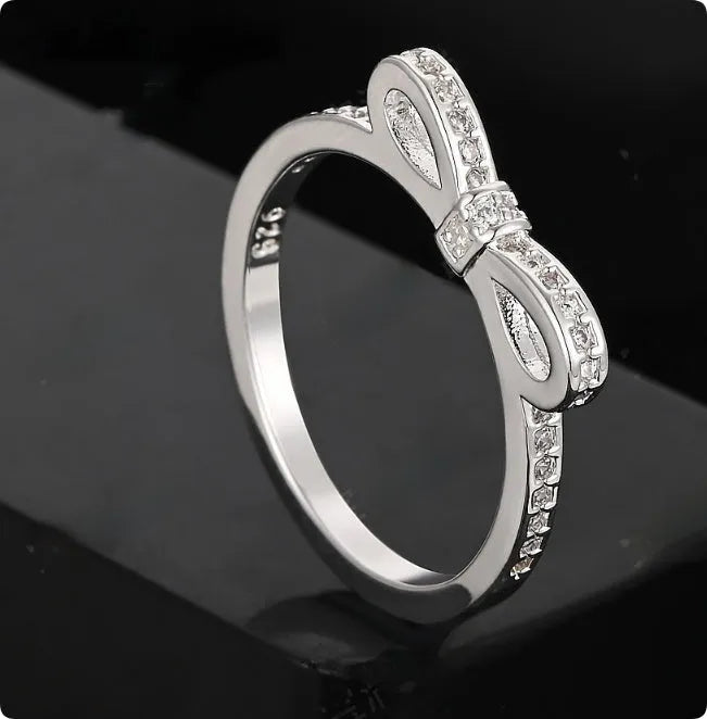 A silver couple-style ring with a bow shape decorated with rhinestones and zircon crystals.