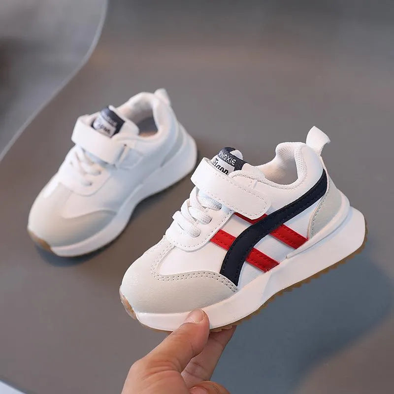 A pair of children's casual sneakers with a Velcro strap, shown in a neutral solid colour.