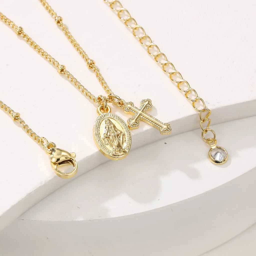 Geometric gold Virgin Mary cross pendant necklace on a chain.