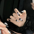 Hand-painted black artificial nails with pink hearts and a bow design, showing mid-length cat's eye style.