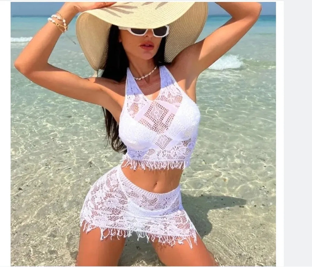 Women's white two-piece bikini with lace cover-up skirt and tassel trim on a beach.