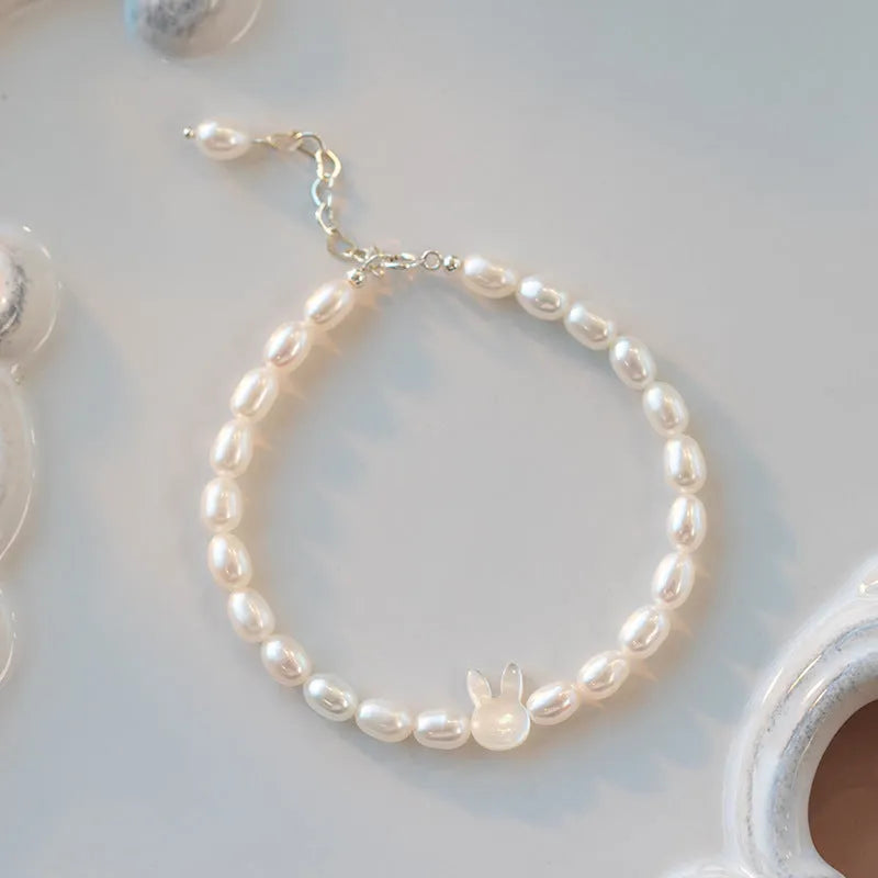 White pearl and silver rabbit charm bracelet on a stretched elastic string showing its adjustable fit.