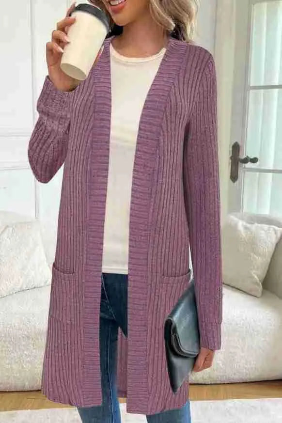 A woman wearing a loose grey knitted cardigan jacket with long sleeves and patch pockets.
