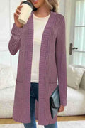A woman wearing a loose grey knitted cardigan jacket with long sleeves and patch pockets.