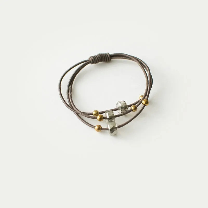 Crystal string beads rubber knotted hair band with octagonal electroplated beads in matte golden, on a plain background.