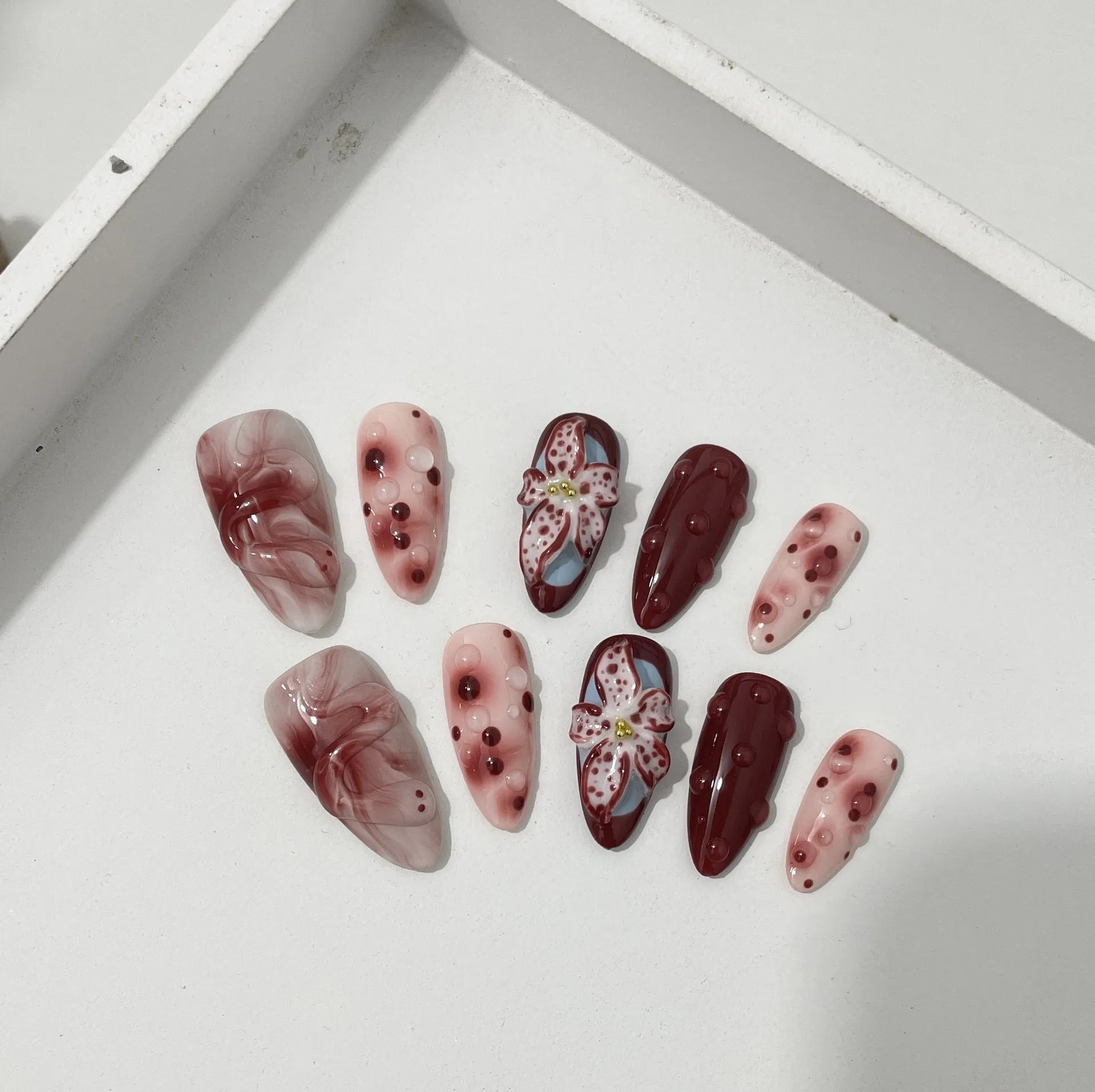 Set of almond-coloured artificial nails with hand-painted rose and 3D carved butterfly designs, showing short and medium lengths.