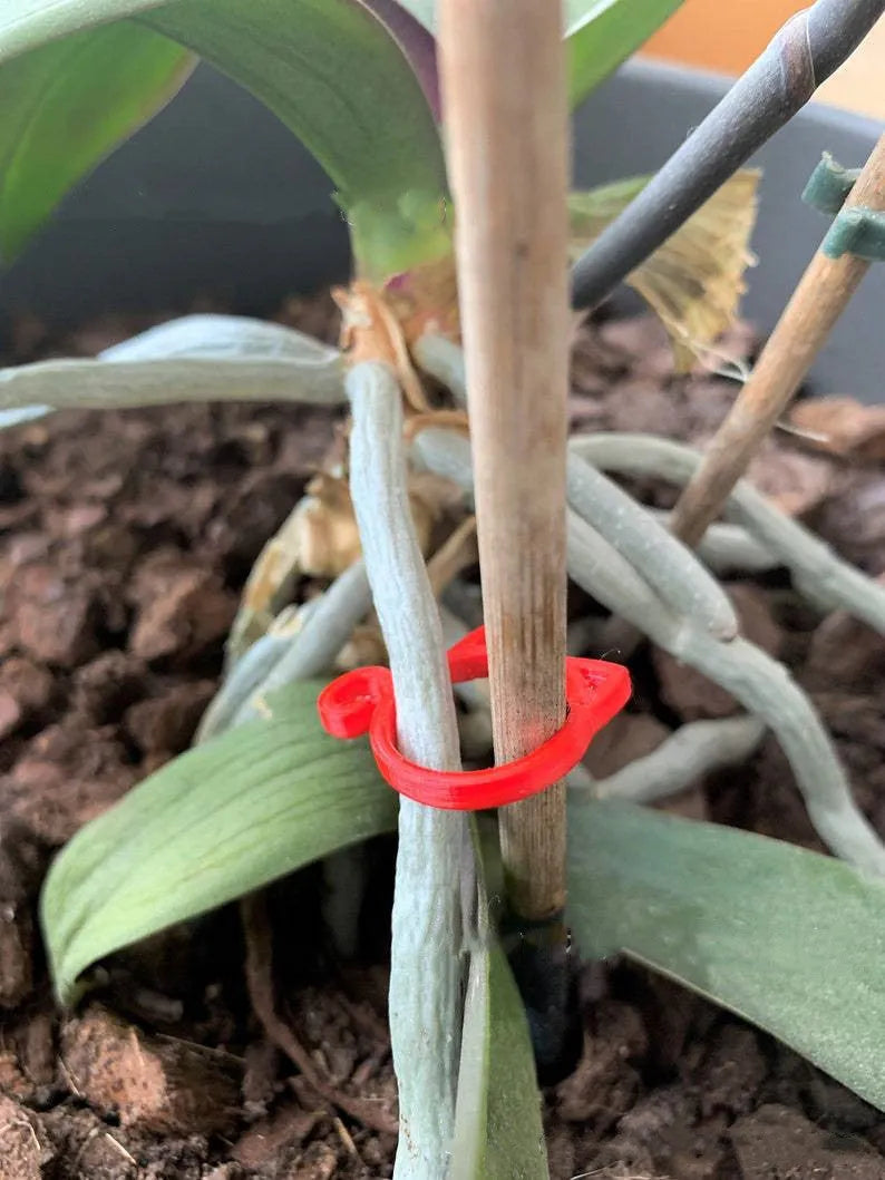 A red cat-shaped plastic clip for holding plant stems against a support stake.