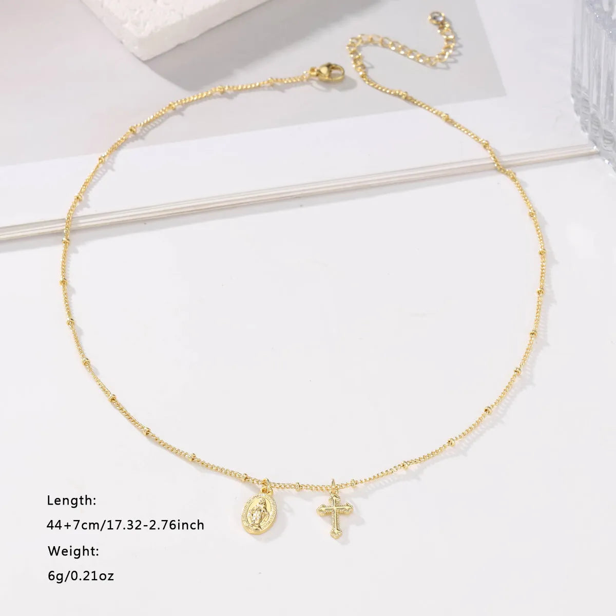 Geometric gold Virgin Mary cross pendant necklace on a chain.
