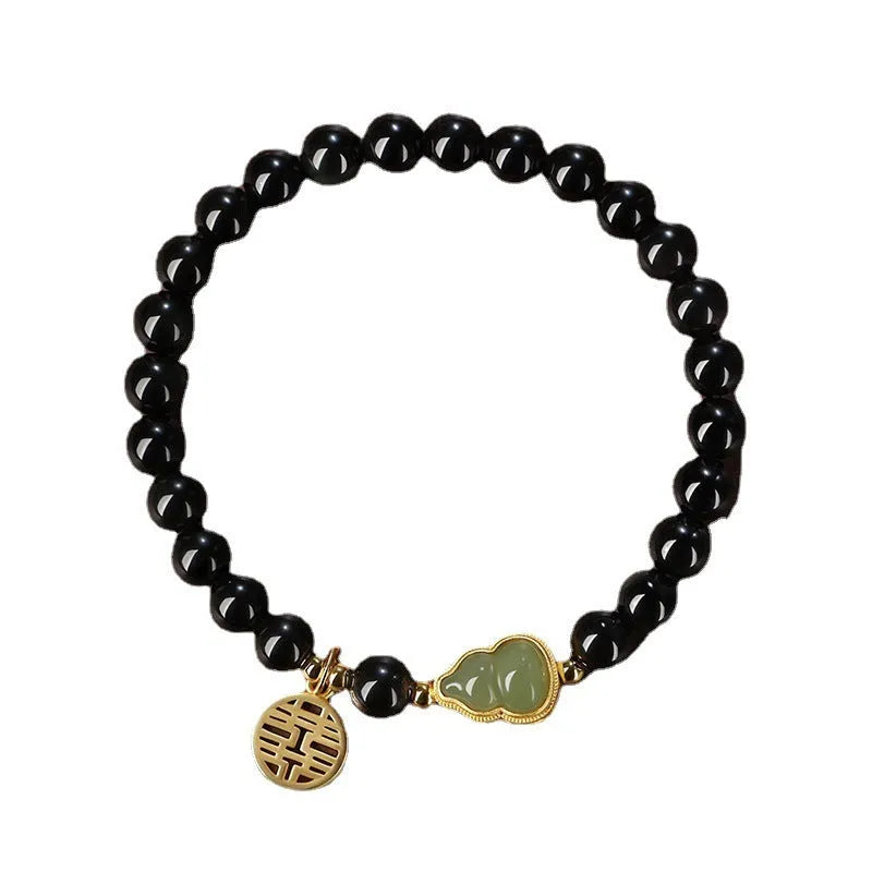 Black obsidian bracelet with a green Hetian jade gourd charm on a wrist.