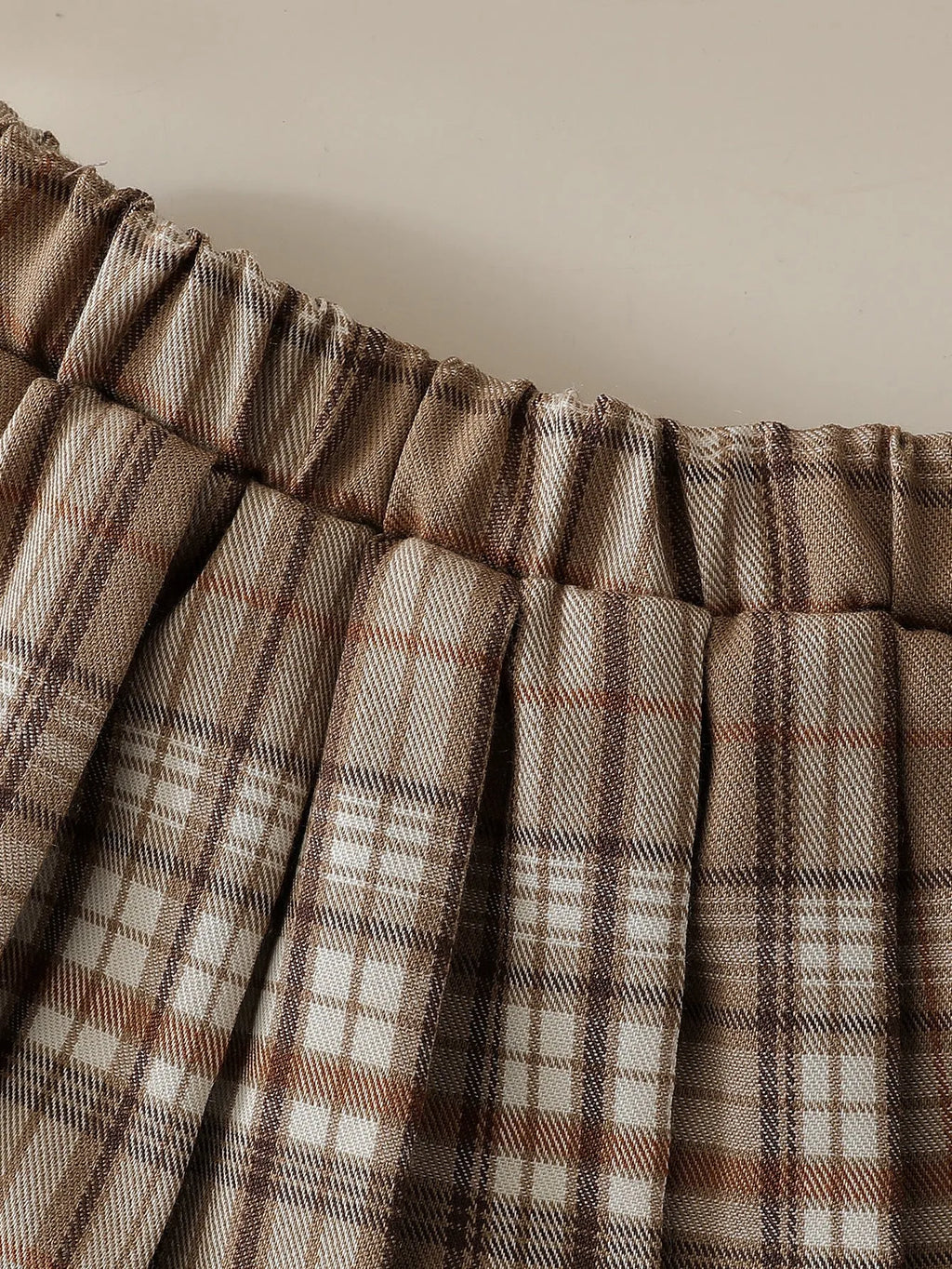 Girls' light brown plaid three-piece set with top, knitted vest, and pleated skirt on white background