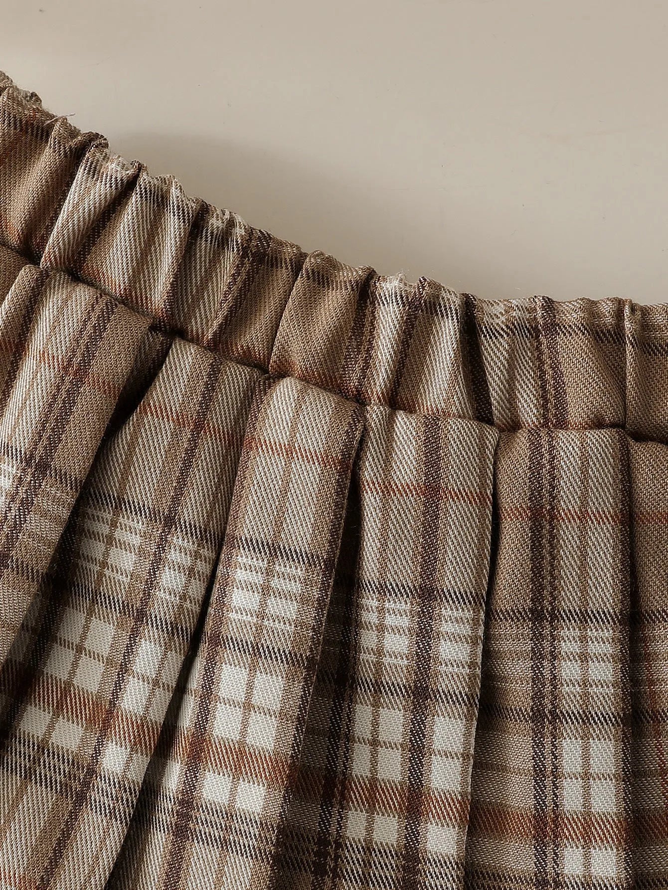 Girls' light brown plaid three-piece set with top, knitted vest, and pleated skirt on white background