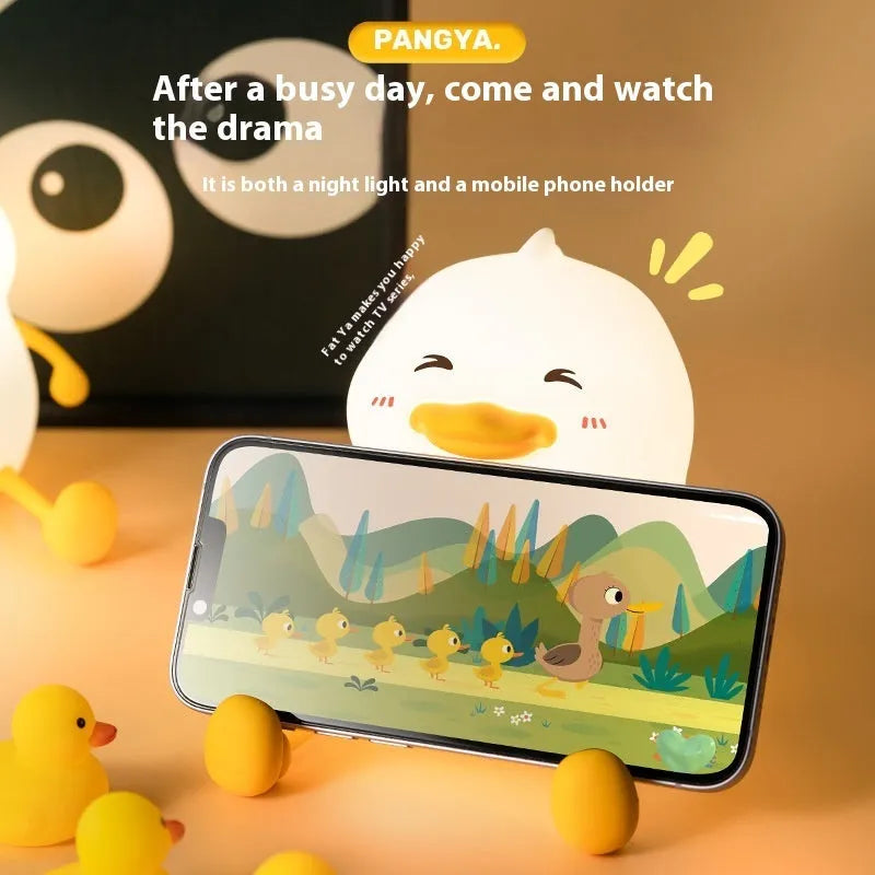 Chubby silicone pat night light on desk holding a mobile phone, showing soft glow.