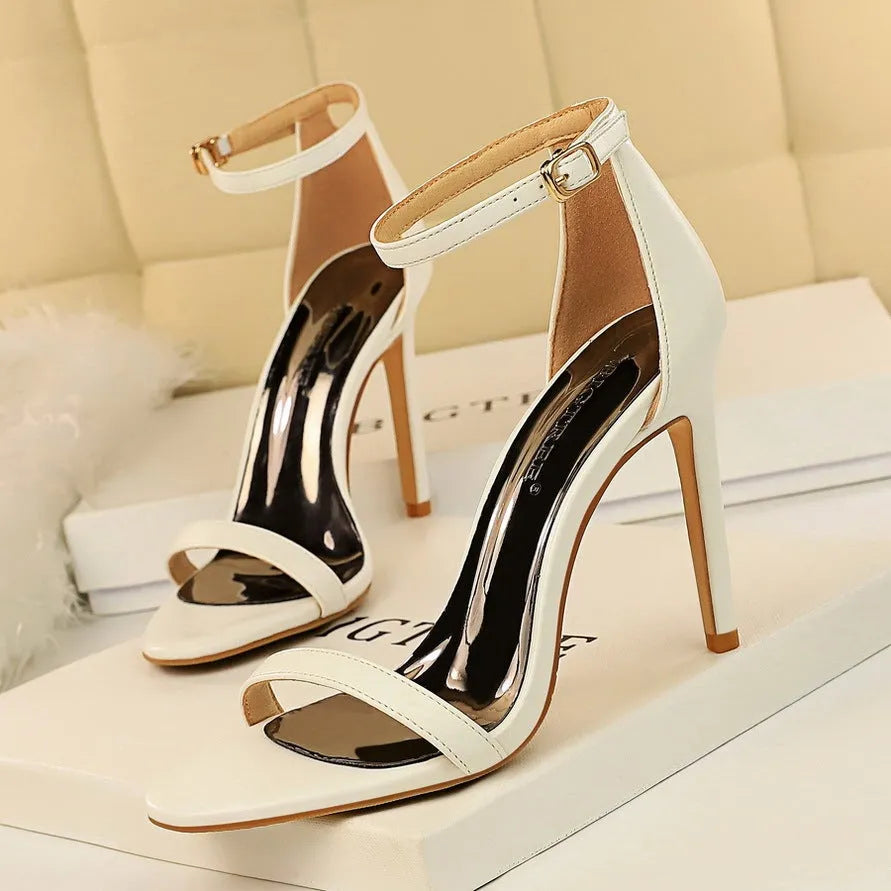 White ankle-strap high heel with open toe and silver buckle on a plain background