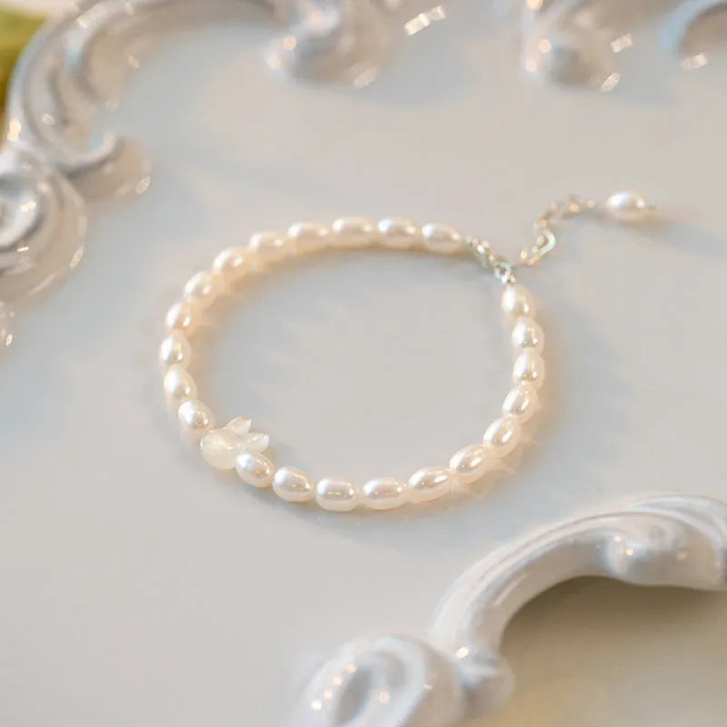 White pearl and silver rabbit charm bracelet on a stretched elastic string showing its adjustable fit.