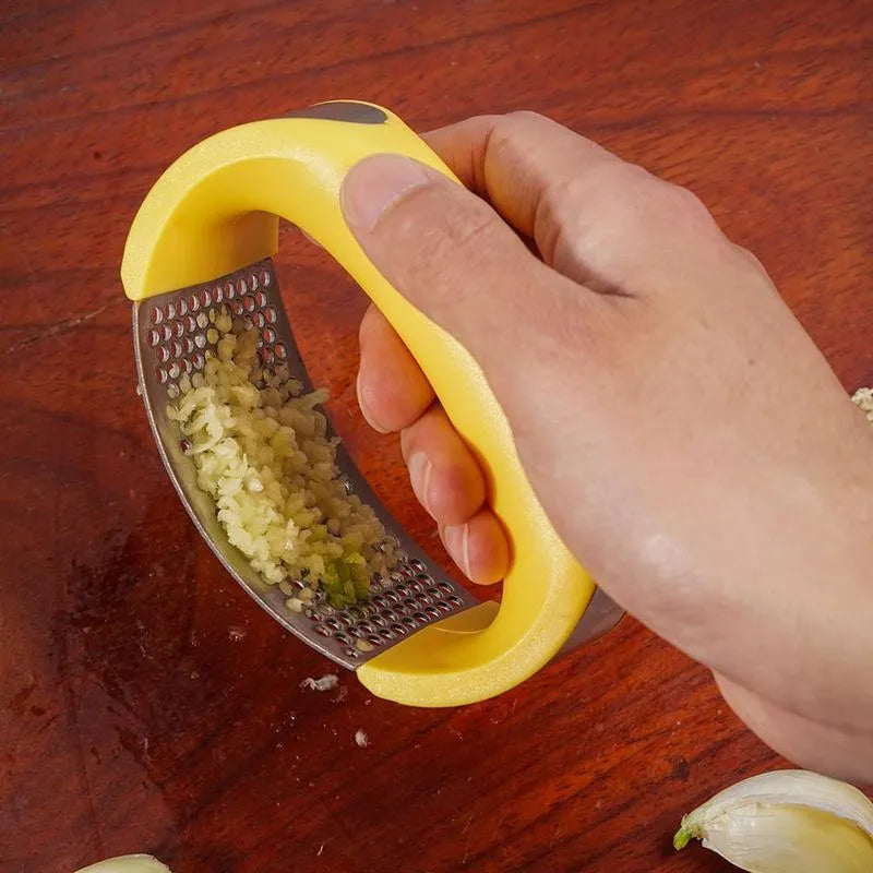 Stainless steel garlic press with ergonomic black handle on a kitchen counter.