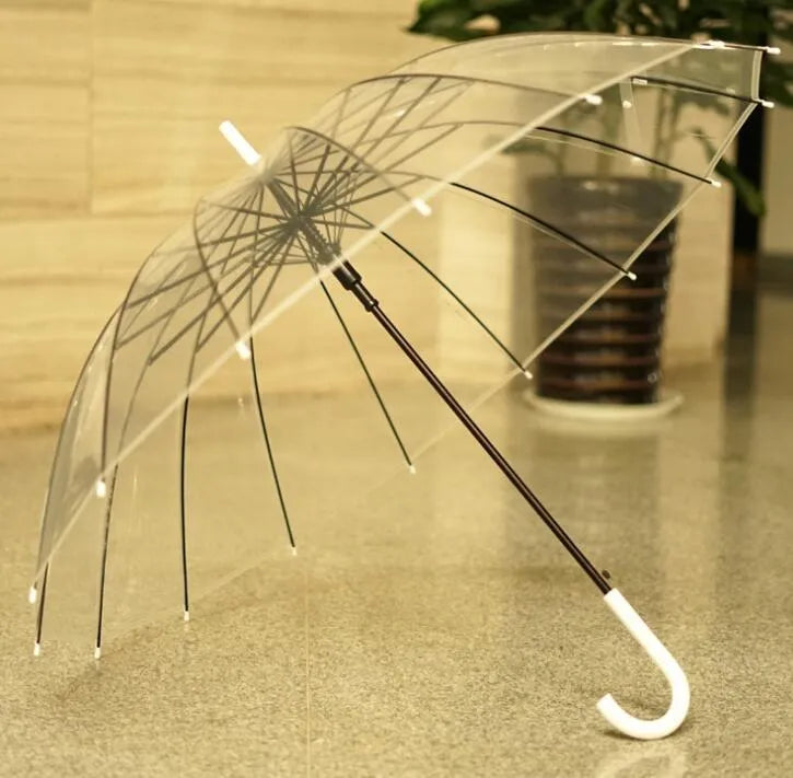 Long-handled transparent umbrella with black steel frame and white handle on a black background.