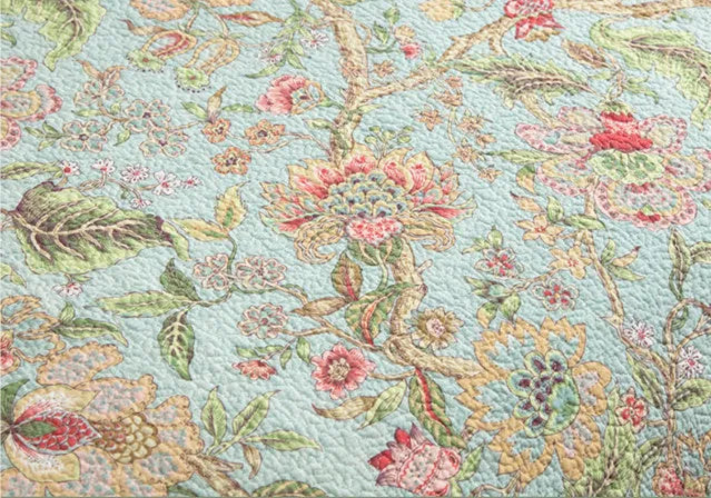 Blue American floral and bird pattern quilted cotton bedspread laid flat on a bed.
