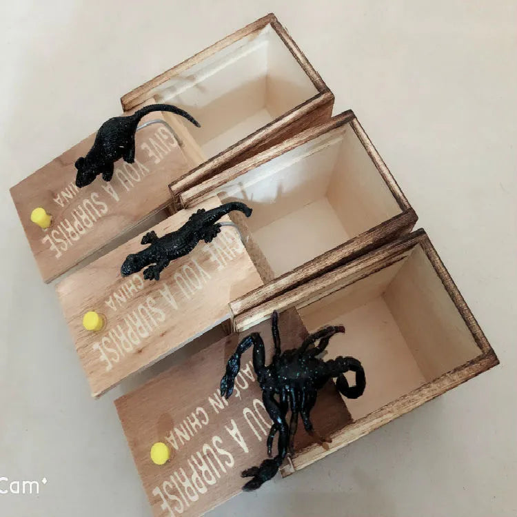 Wooden prank scare box open showing a lifelike spider figurine on a spring, next to the box lid.