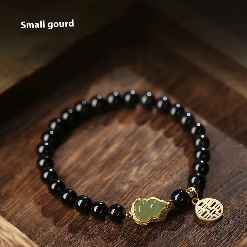 Black obsidian bracelet with a green Hetian jade gourd charm on a wrist.