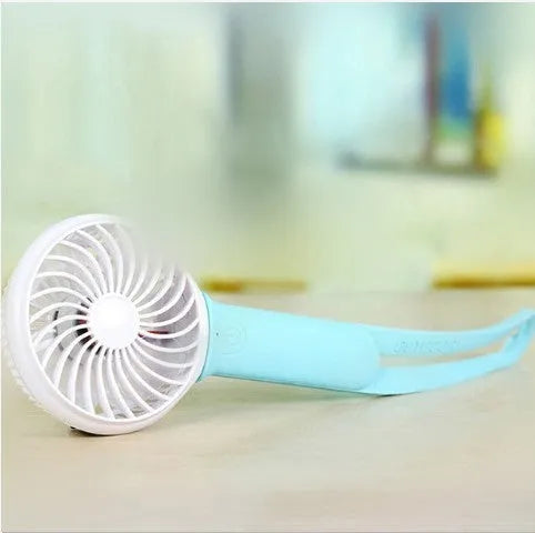 Mini USB desk fan with blue blades and housing on a wooden desk, showing LED light and speed buttons.