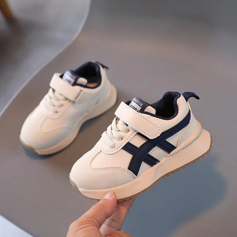 A pair of children's casual sneakers with a Velcro strap, shown in a neutral solid colour.