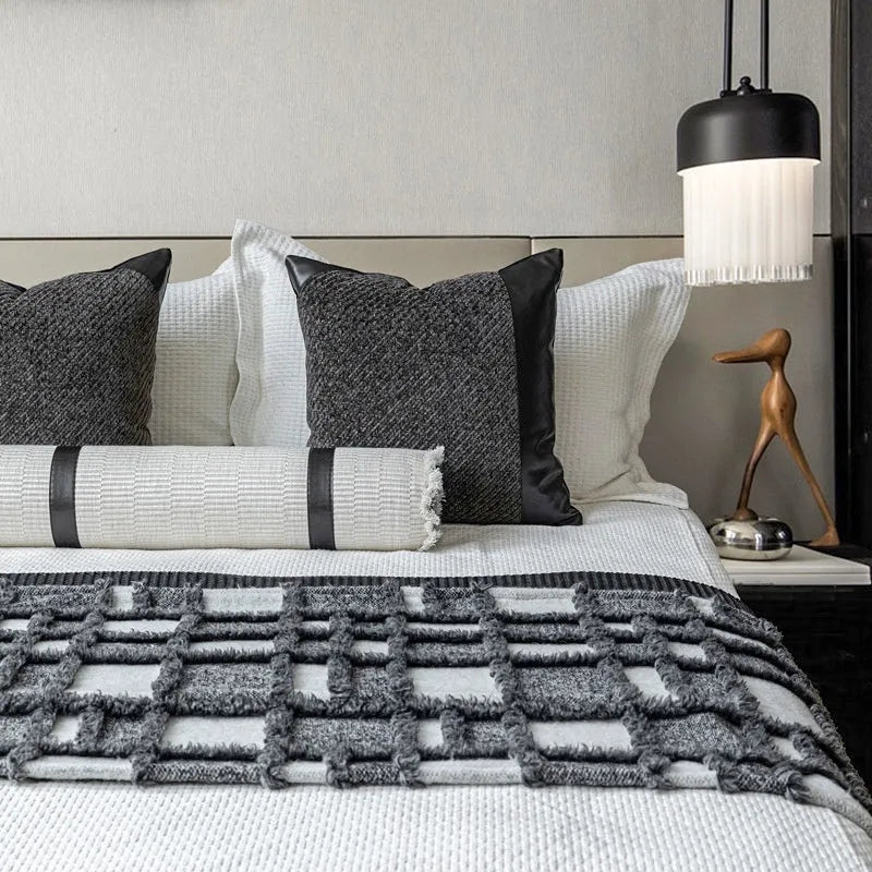 Modern minimalist grey and white plaid bed runner blanket set with matching pillowcase and leather round pillow on a bed.