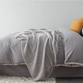 Small grey polyester nap blanket folded on a sofa, showing its 127x170cm size.