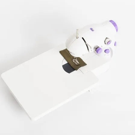 Miniature white and grey electric household sewing machine with thread spool and power cord.