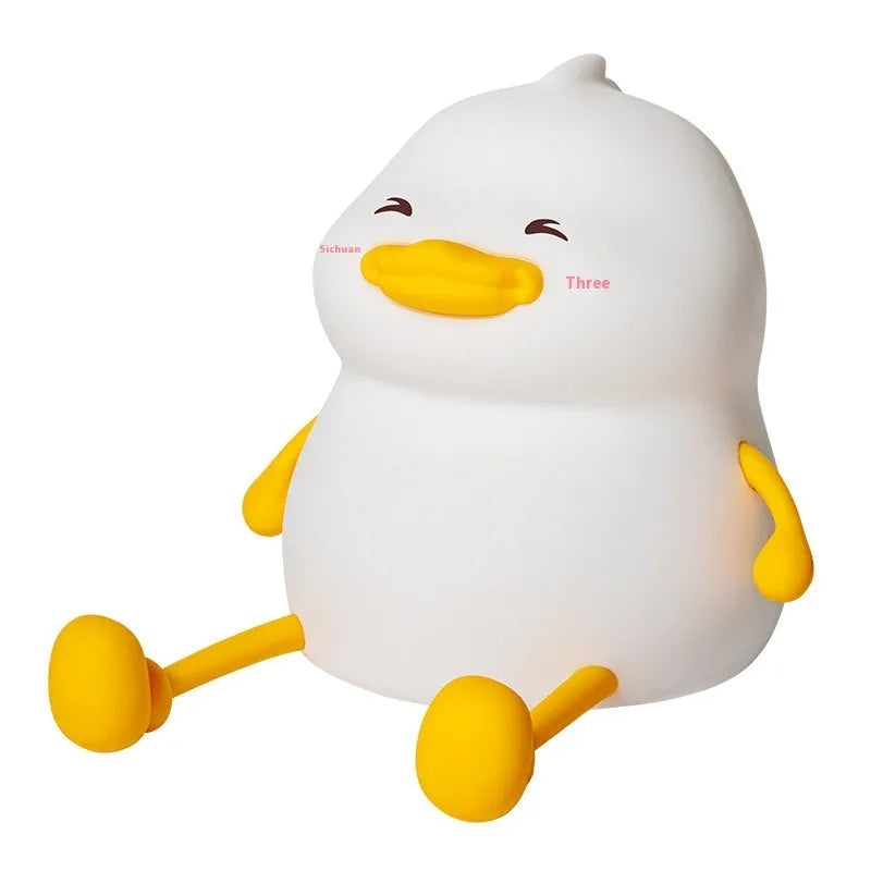 Chubby silicone pat night light on desk holding a mobile phone, showing soft glow.