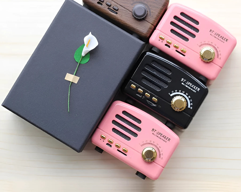 Compact vintage wood style Bluetooth speaker in pink, black, or wood grain finish on a table.
