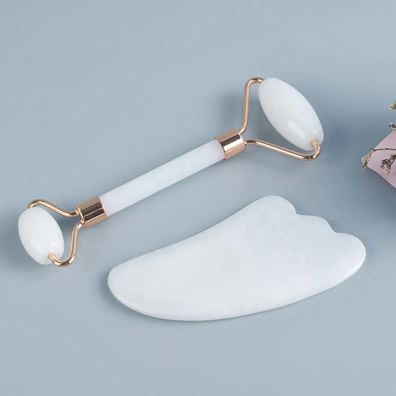 White jade double-headed facial roller and scraping board set on a flat surface.