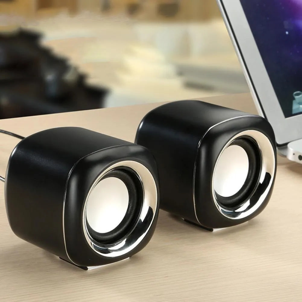 Pair of compact black wired desktop computer speakers with 3.5mm plug next to a laptop.