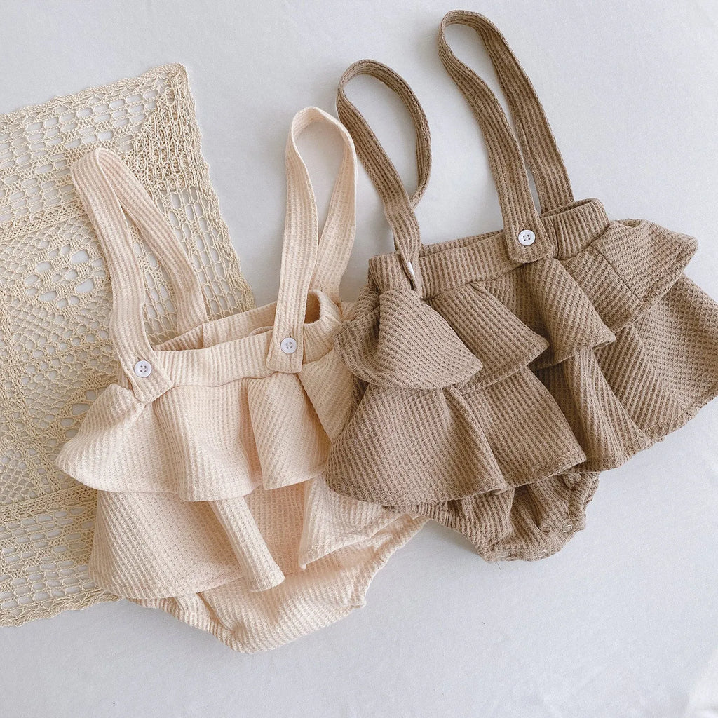 Baby girl wearing a cotton romper with a pleated lotus leaf sling and triangle climb design in apricot colour.