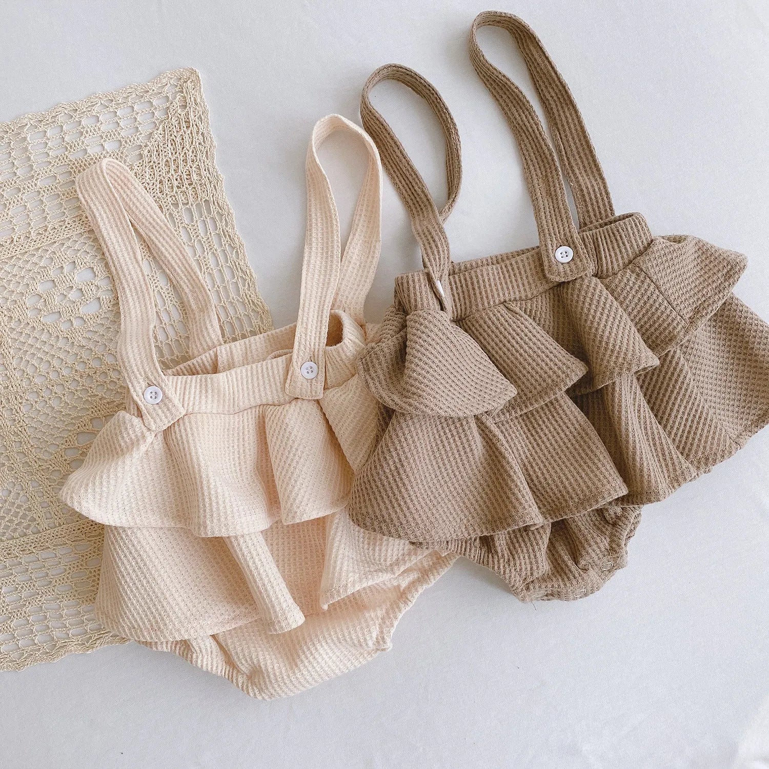 Baby girl wearing a cotton romper with a pleated lotus leaf sling and triangle climb design in apricot colour.