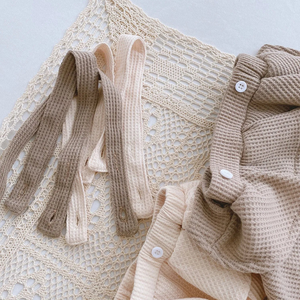 Baby girl wearing a cotton romper with a pleated lotus leaf sling and triangle climb design in apricot colour.