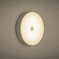Small white USB rechargeable motion sensor LED night light with adhesive tape for mounting.