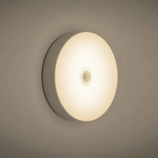 Small white USB rechargeable motion sensor LED night light with adhesive tape for mounting.