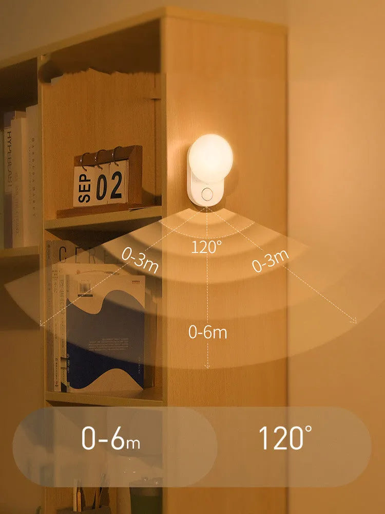 White USB rechargeable sensor night light with warm LED glow, shown on a bedroom nightstand.
