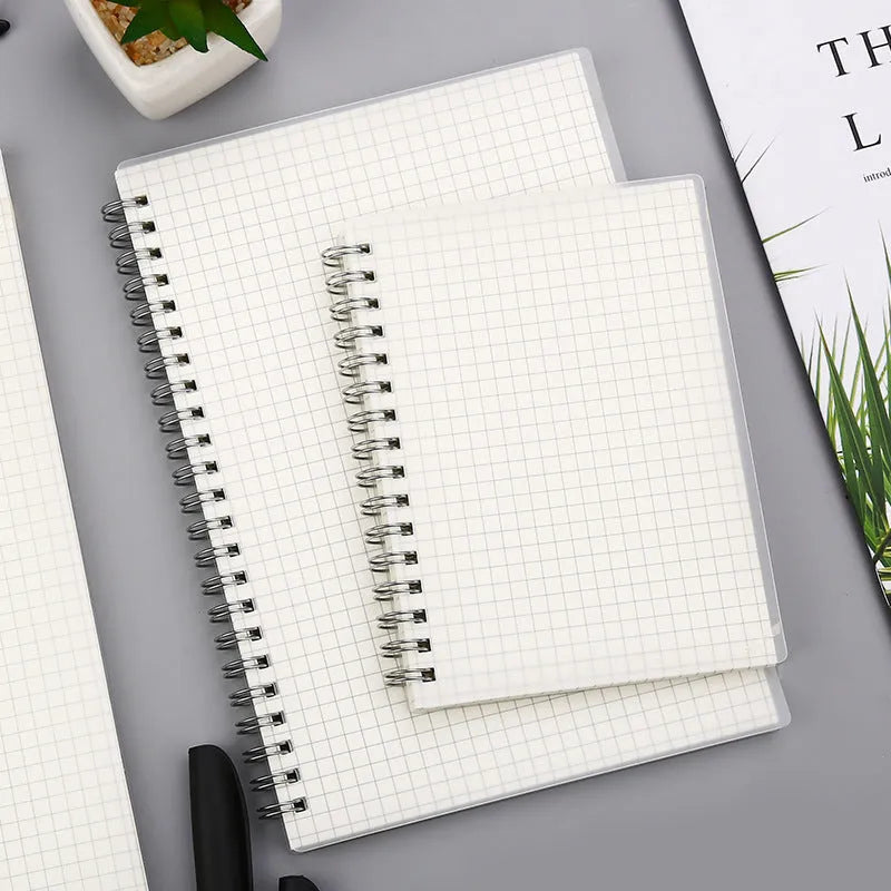 Coil-bound notebook with grid dot matrix ruling in A6, A5, and B5 sizes on a desk.