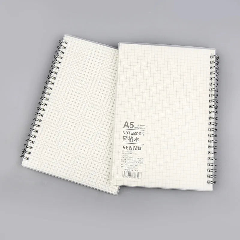 Coil-bound notebook with grid dot matrix ruling in A6, A5, and B5 sizes on a desk.