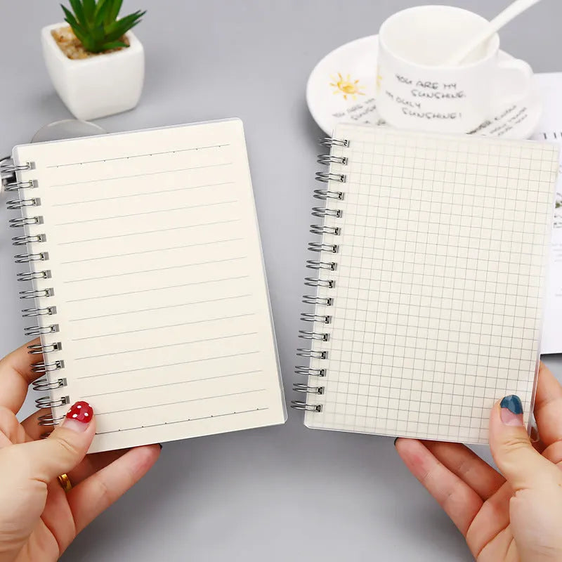 Coil-bound notebook with grid dot matrix ruling in A6, A5, and B5 sizes on a desk.