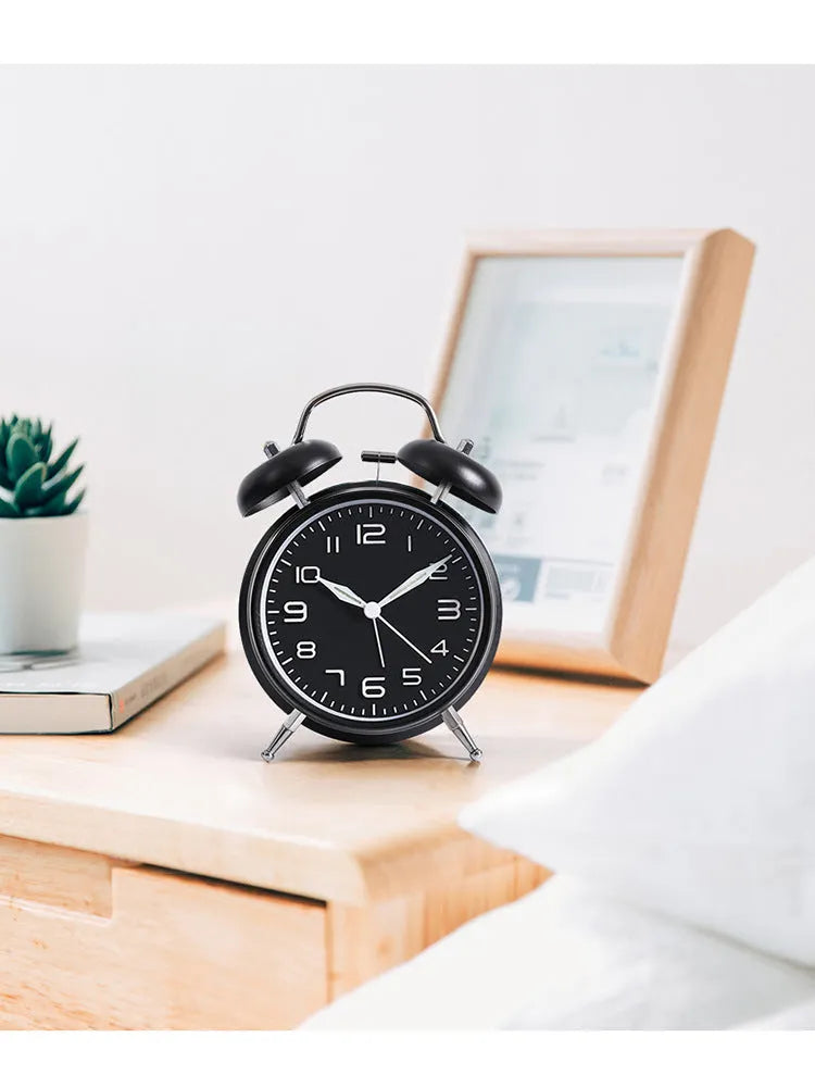 Large black metal alarm clock with luminous display and silent sweep movement on a bedside table