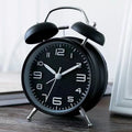 Large black metal alarm clock with luminous display and silent sweep movement on a bedside table