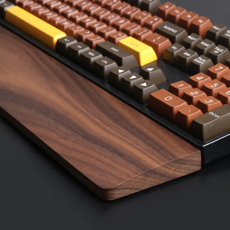 Solid walnut wood wrist rest for a mechanical keyboard on a desk.