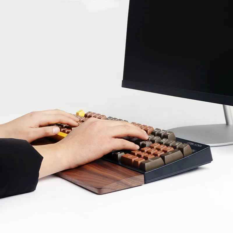 Solid walnut wood wrist rest for a mechanical keyboard on a desk.