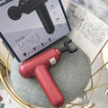 Black handheld fascia gun massager with metal head on a grey background.