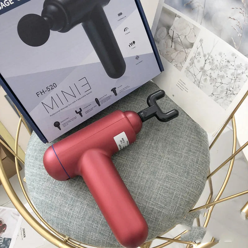 Black handheld fascia gun massager with metal head on a grey background.