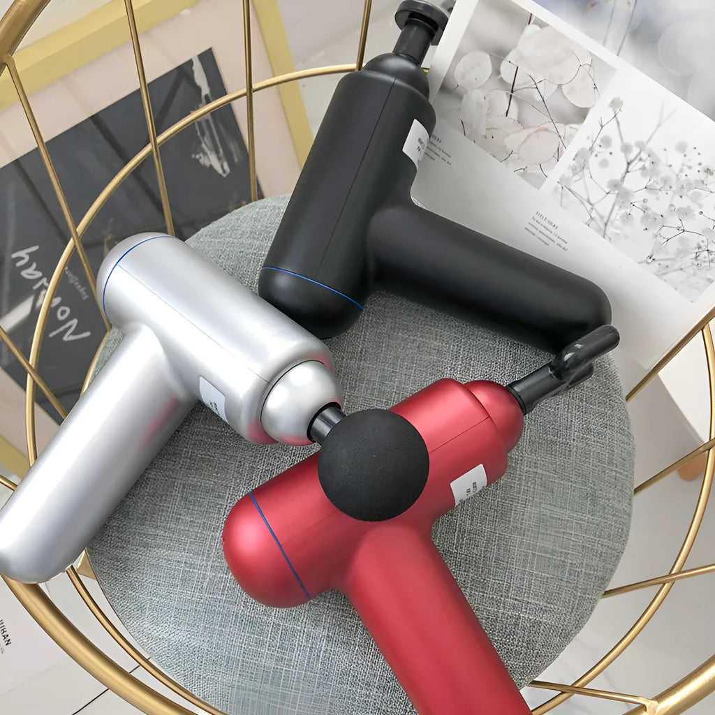 Black handheld fascia gun massager with metal head on a grey background.