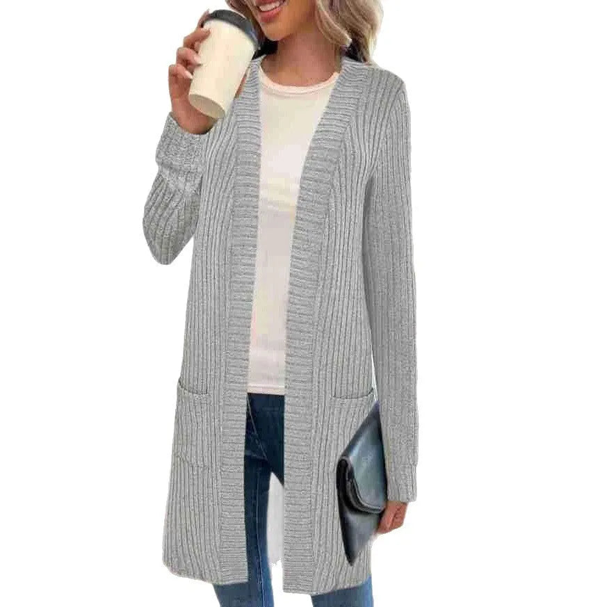 A woman wearing a loose grey knitted cardigan jacket with long sleeves and patch pockets.