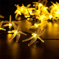 Outdoor solar-powered dragonfly string lights with garden spike, shown in a warm white glow